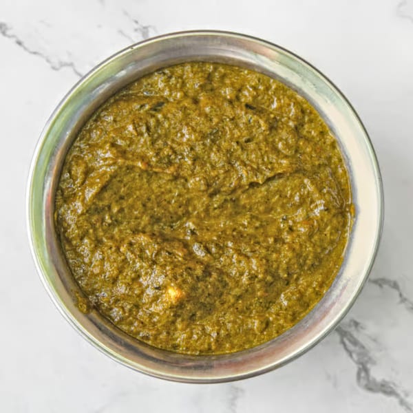 Overhead view of a metal bowl filled with vibrant green Indian Saag Paneer on a white marble surface.
