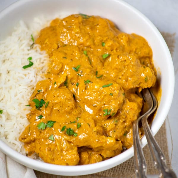 A white bowl filled with Colorado Curry Berthoud's Indian butter chicken and white rice, garnished with cilantro.