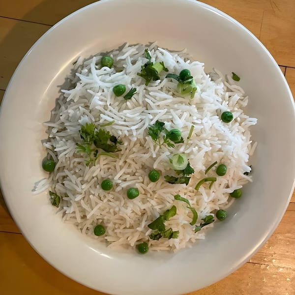 A white bowl of fluffy basmati rice, garnished with green peas and fresh cilantro.