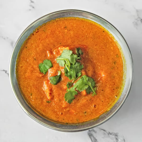Close-up of a vibrant orange Indian curry, garnished with fresh green cilantro in a metal bowl.